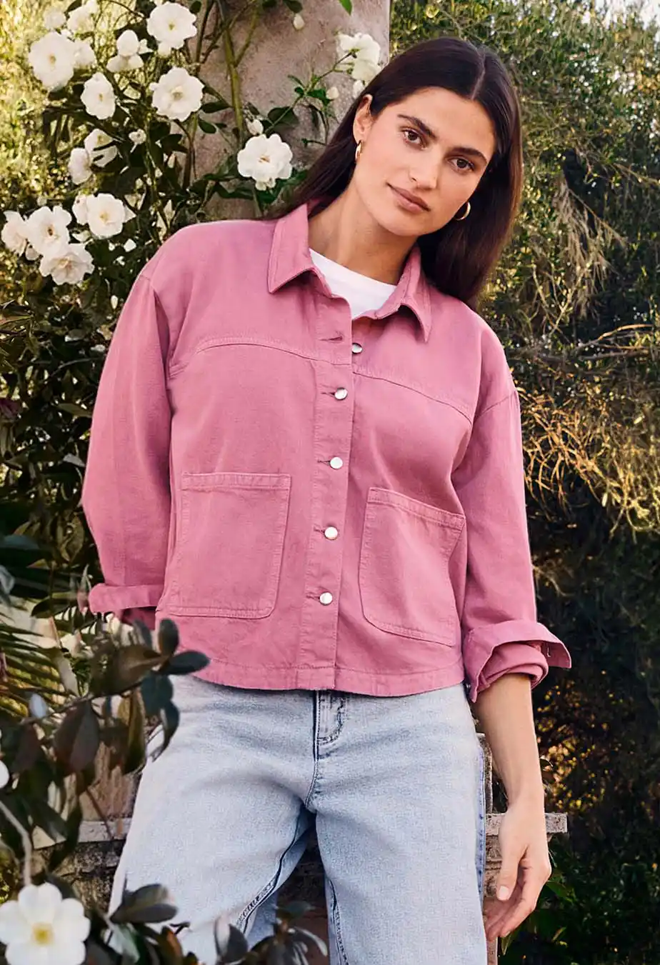Chemise rose avec boutons et poches, T-shirt blanc en dessous, jean de couleur claire pour un look estival.