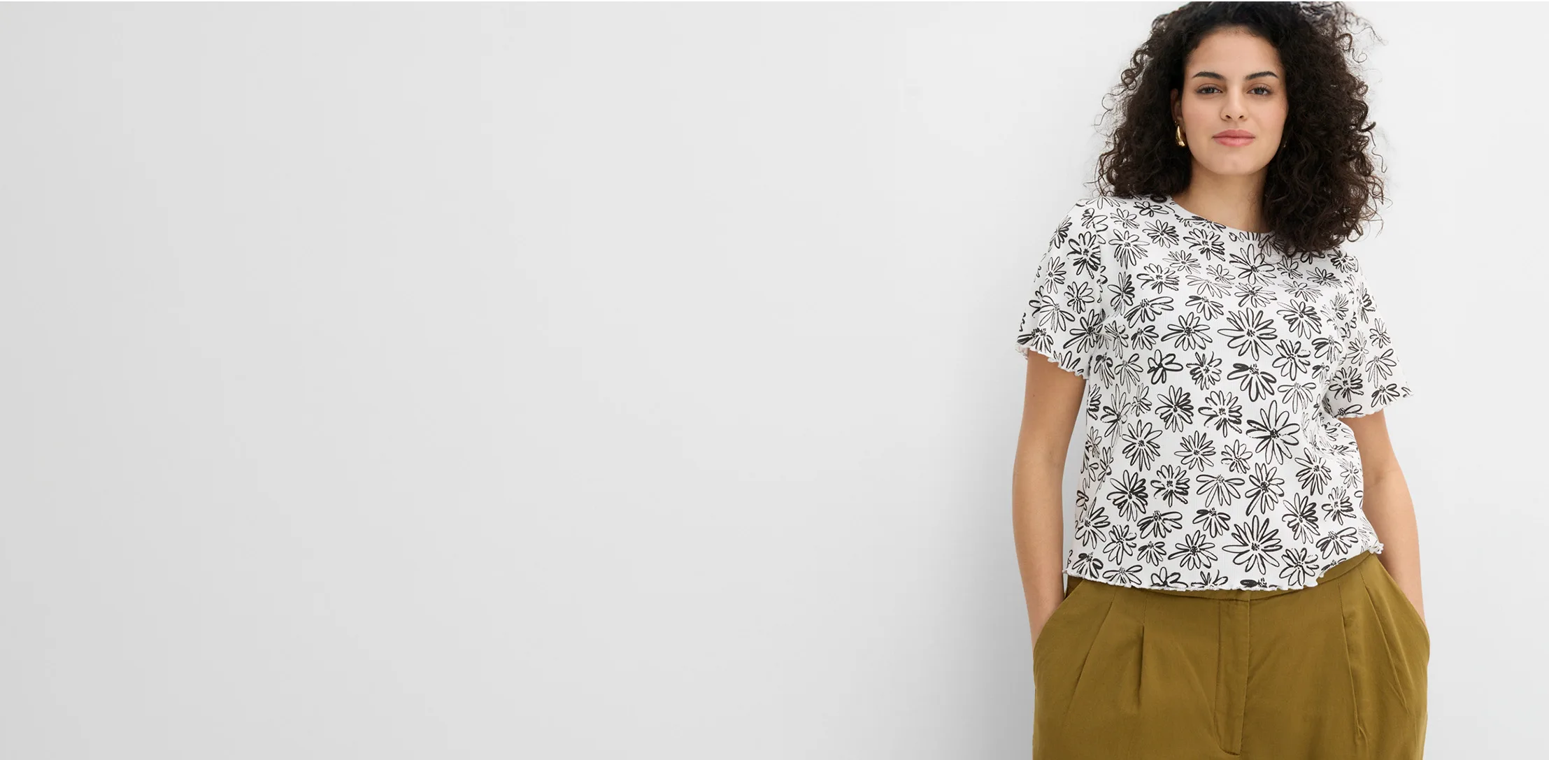 Le mannequin porte un top ample clair à manches courtes, orné d’un motif floral noir.