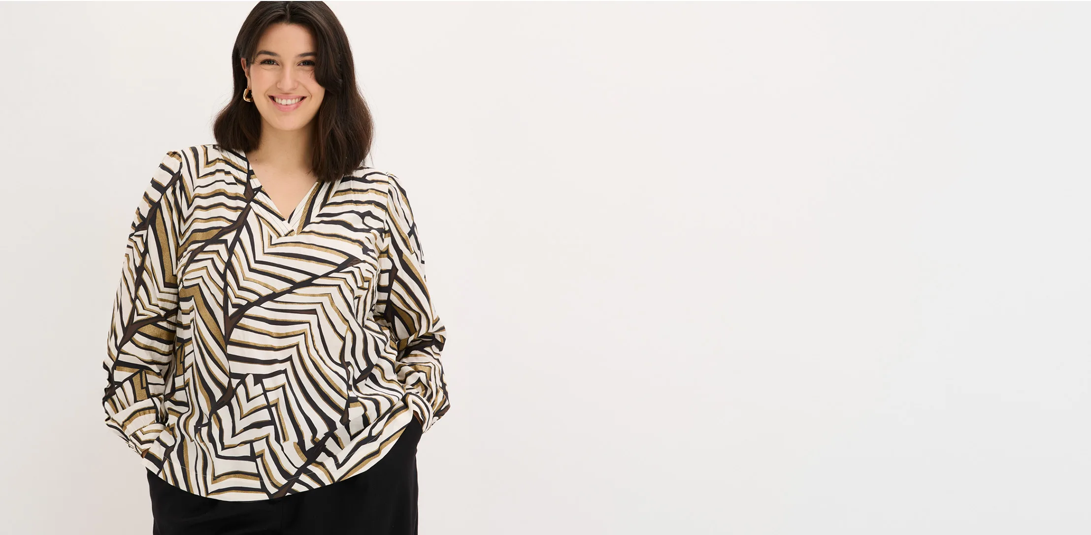Le mannequin porte une blouse ample à manches longues dans des tons beige, noir et blanc, avec un motif géométrique ondulé.