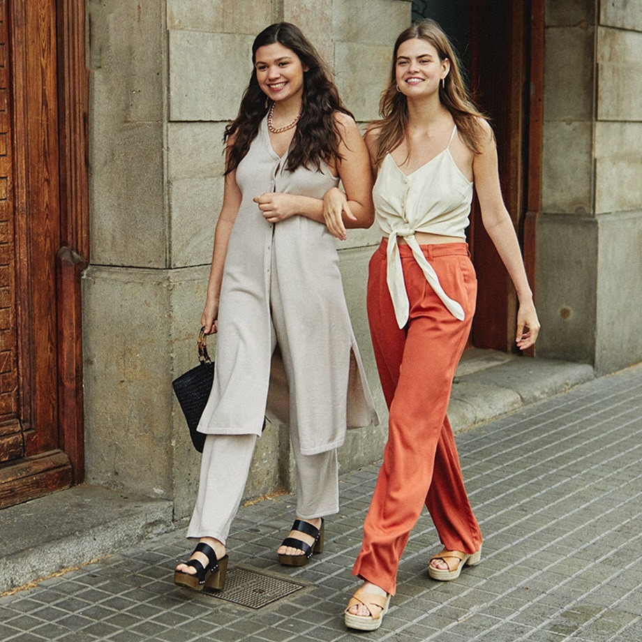 Élégance estivale : tailleurs pantalons de couleur claire et tops fluides, associés à un pantalon orange et des espadrilles.