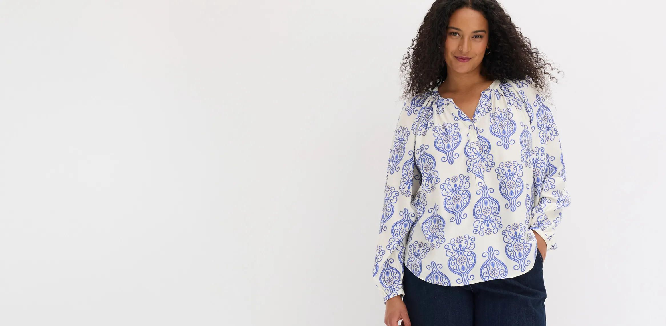 Look élégant avec une blouse blanche à manches longues décorée de motifs bleus et un pantalon foncé.