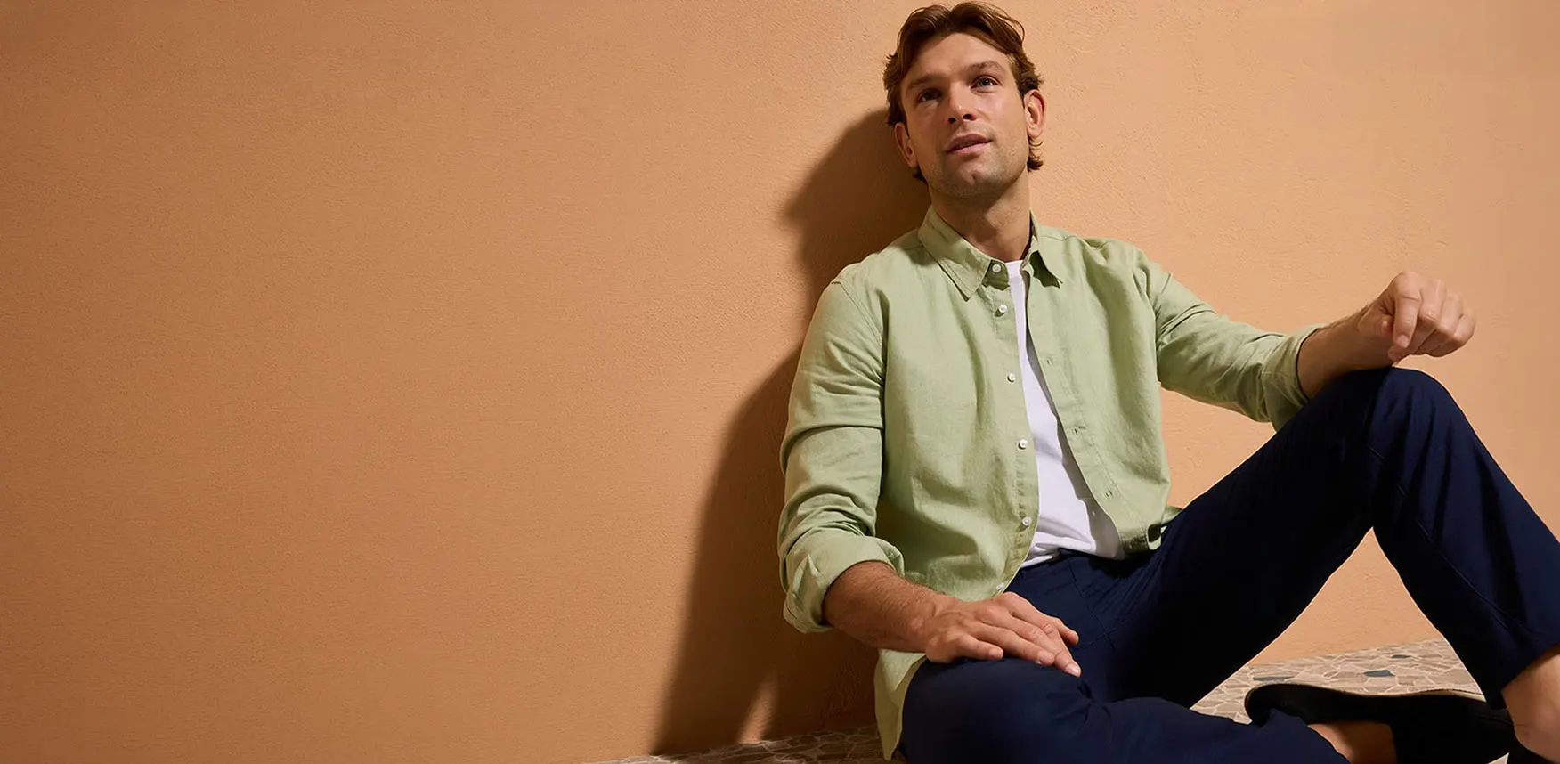 Chemise vert pastel, pantalon bleu foncé et chaussures décontractées.