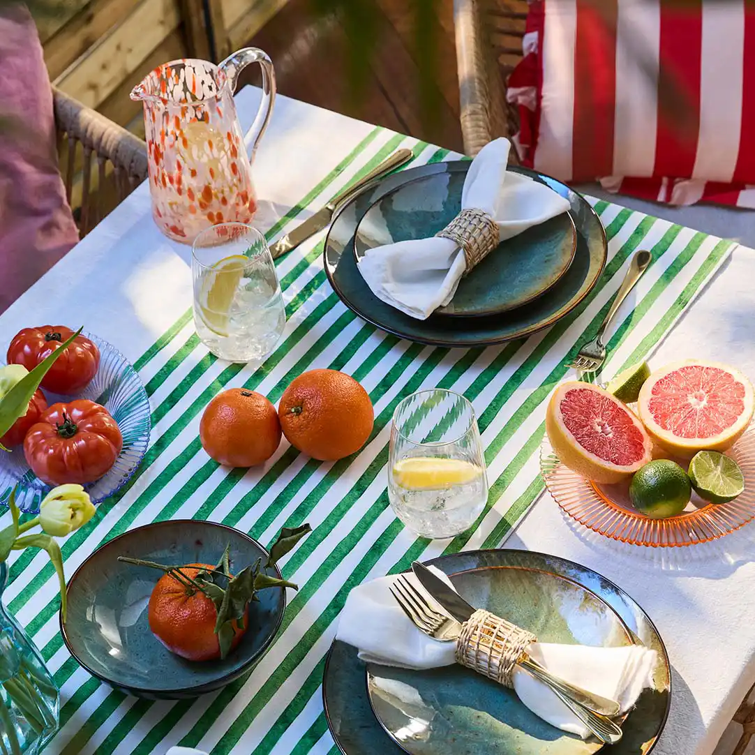Une nappe rayée décore la table estivale sur laquelle sont disposés une vaisselle colorée et des fruits frais.