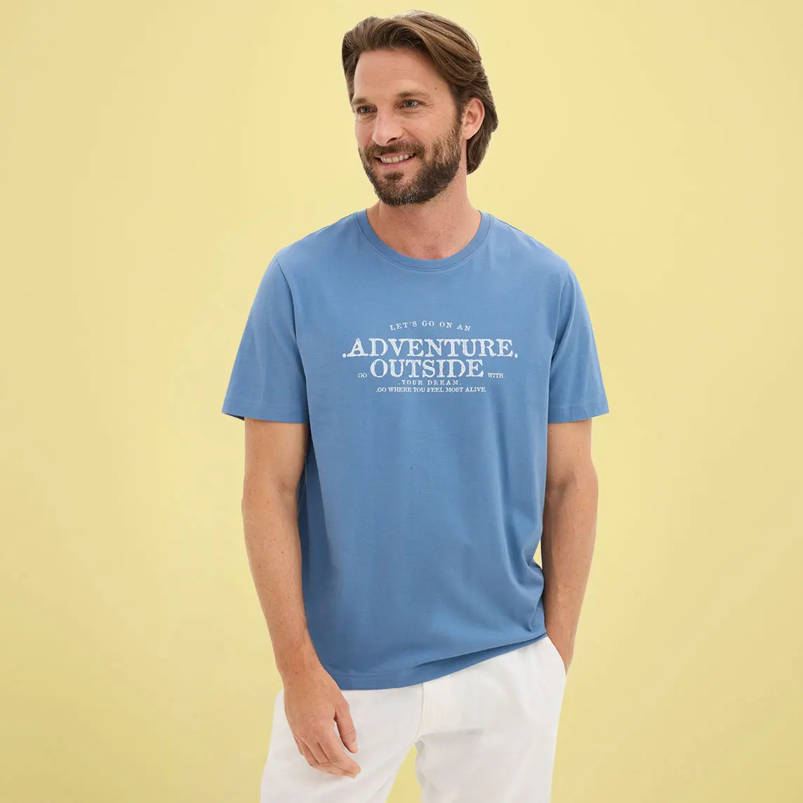 Homme vêtu d'un T-shirt bleu décontracté avec imprimé blanc et d'un pantalon de couleur claire.