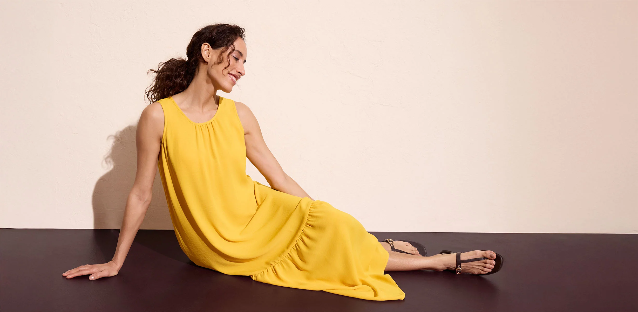 Robe longue jaune sans manches associée à des sandales noires.