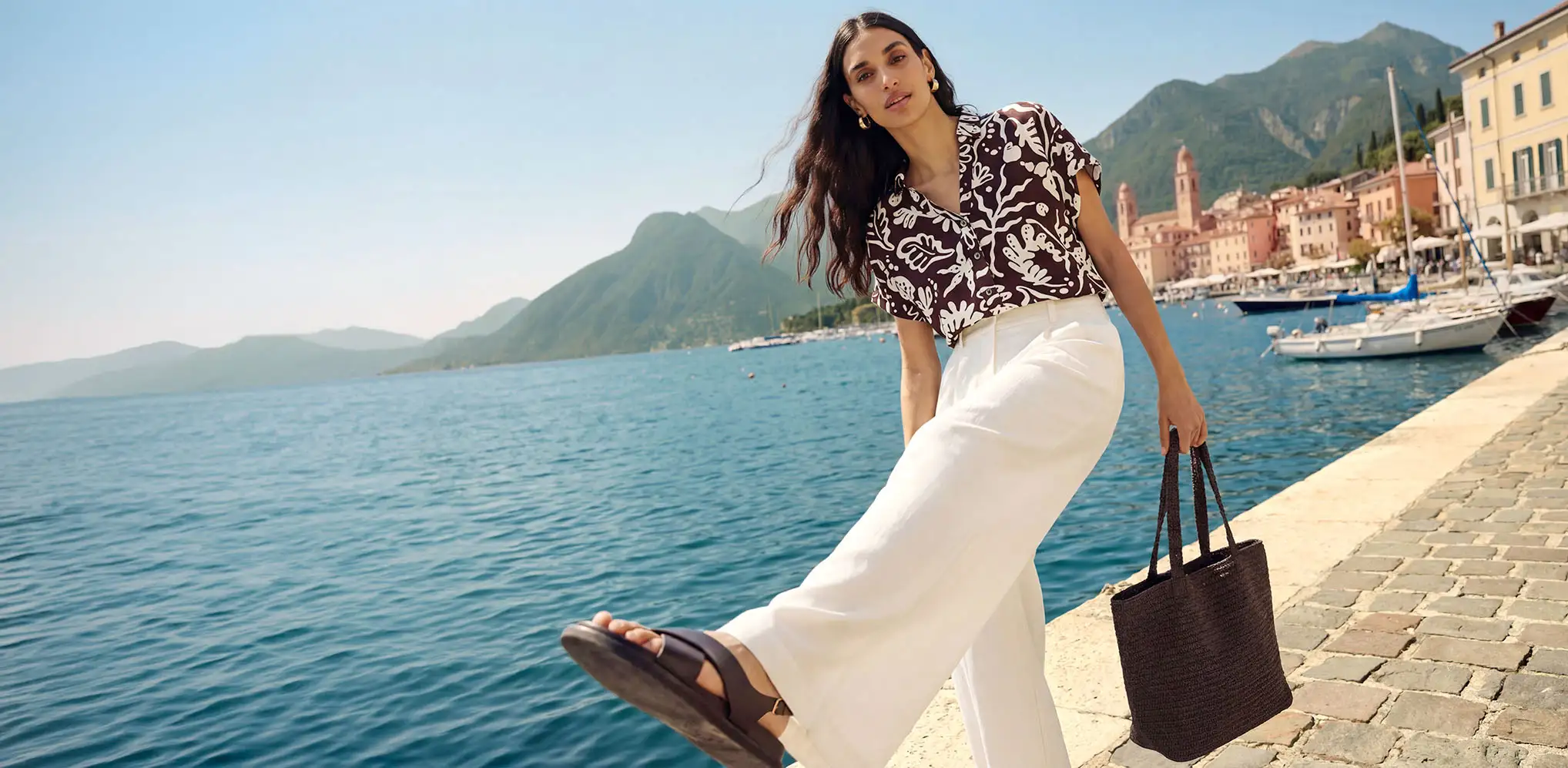 Une femme vêtue d'un pantalon blanc et d'un T-shirt marron imprimé sur le port.