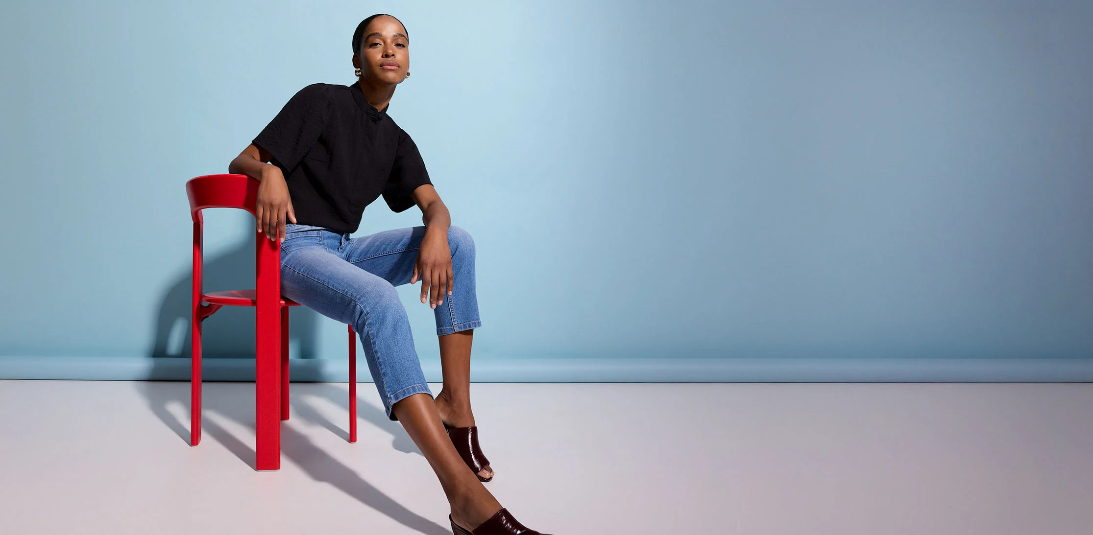 Tenue composée d'un haut noir, un jean bleu et des mules brillantes.
