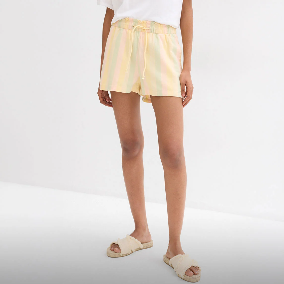 Short rayé pastel, T-shirt blanc et sandales confortables en raphia pour les chaudes journées.