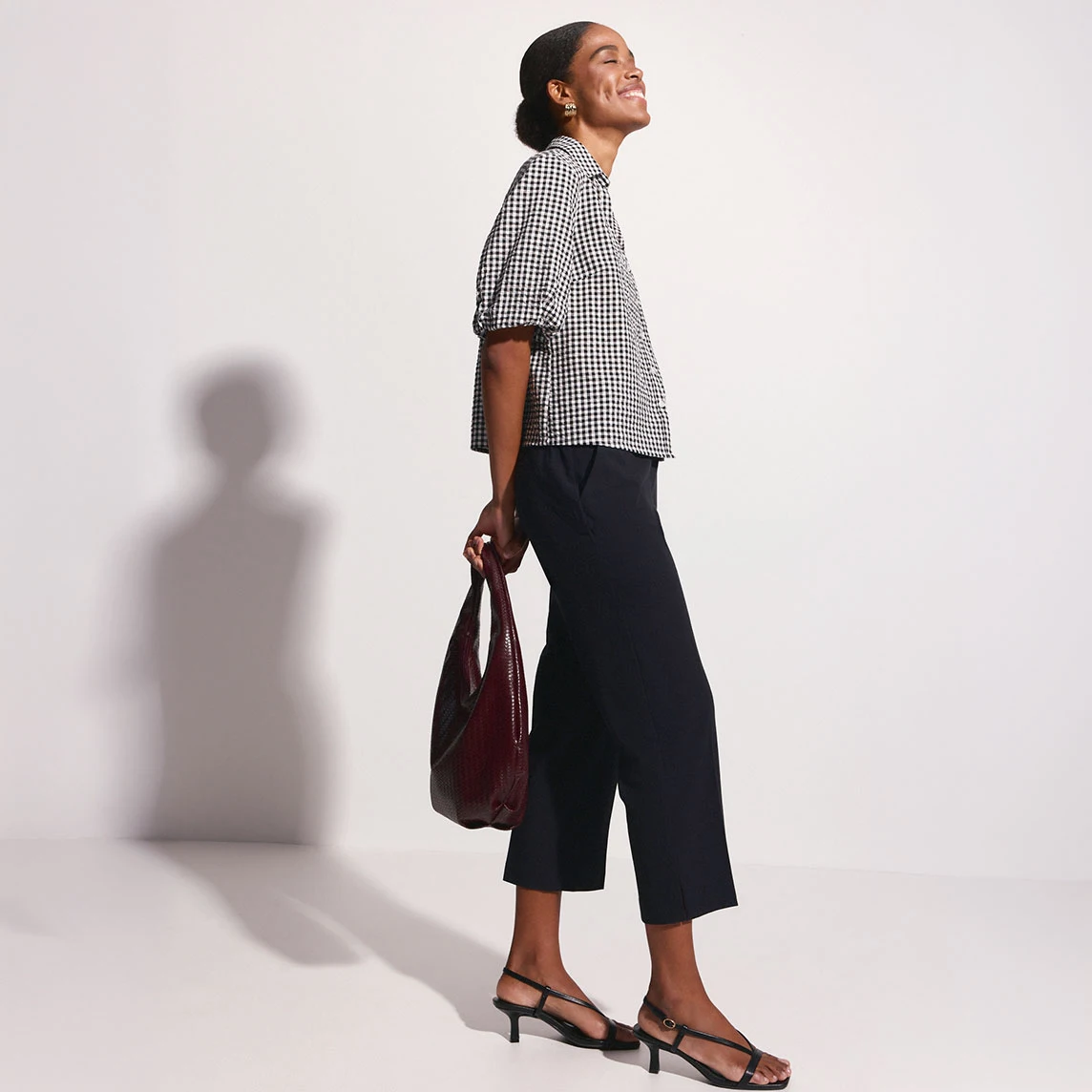 Tenue stylée : chemisier à carreaux, pantalon 3/4 noir, sandales à brides élégantes et sac.
