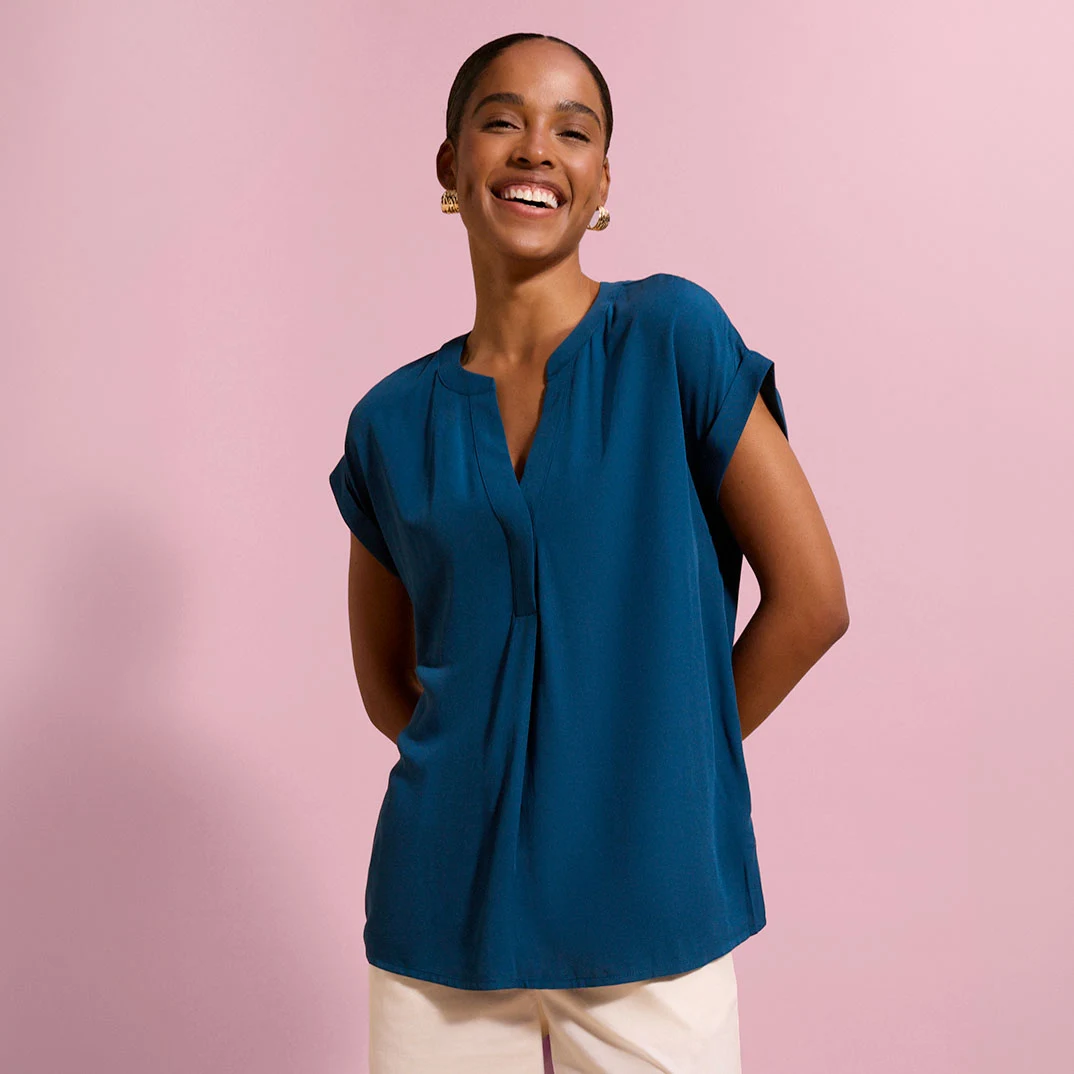 Blouse mode bleu canard avec décolleté en V et manches retroussées, associée à un pantalon de couleur claire.