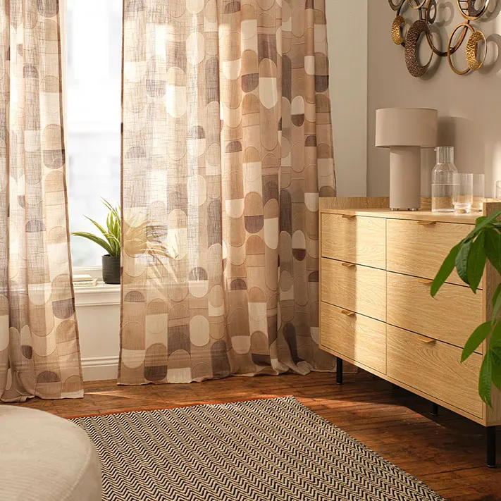 Fenêtres habillées avec un rideau imprimé dans des tons chauds marron et beige.