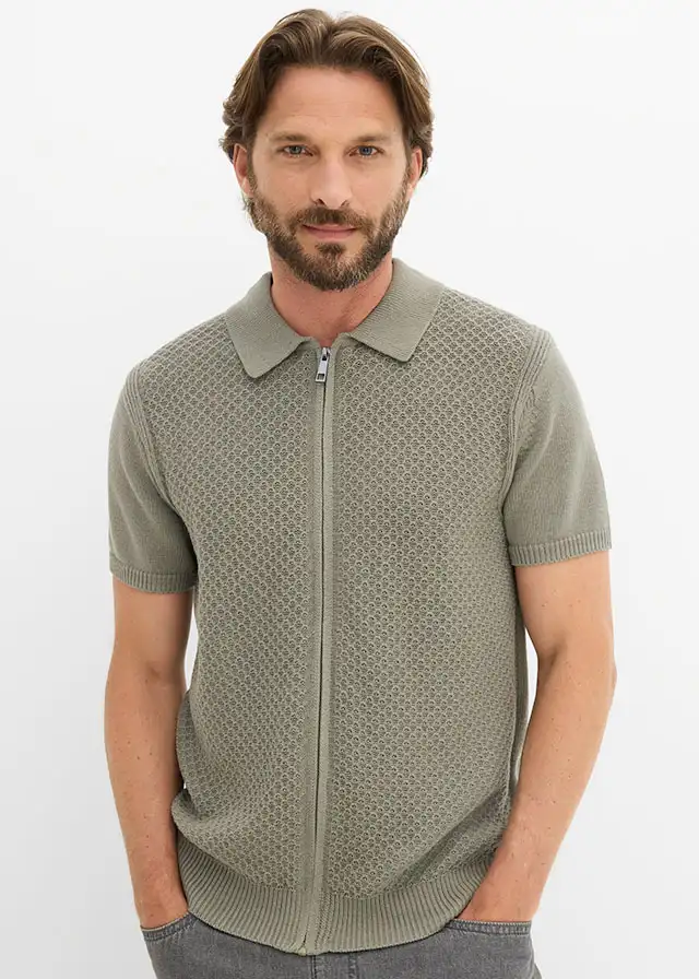 Polo vert en maille avec fermeture zippée et motif structuré, associé à un jean foncé.