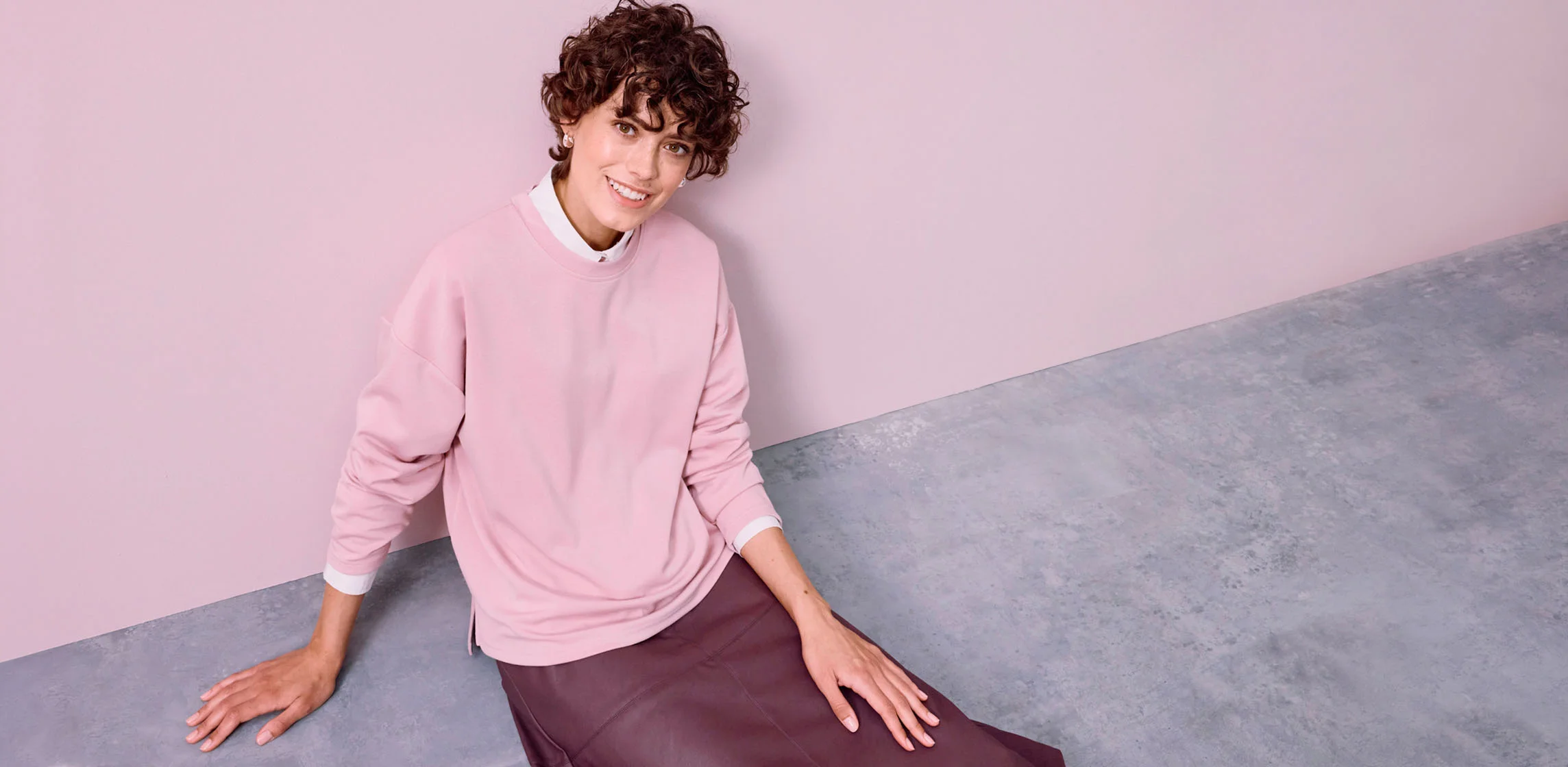 Un sweat rose ample porté sur une chemise blanche, associé à une jupe foncée.