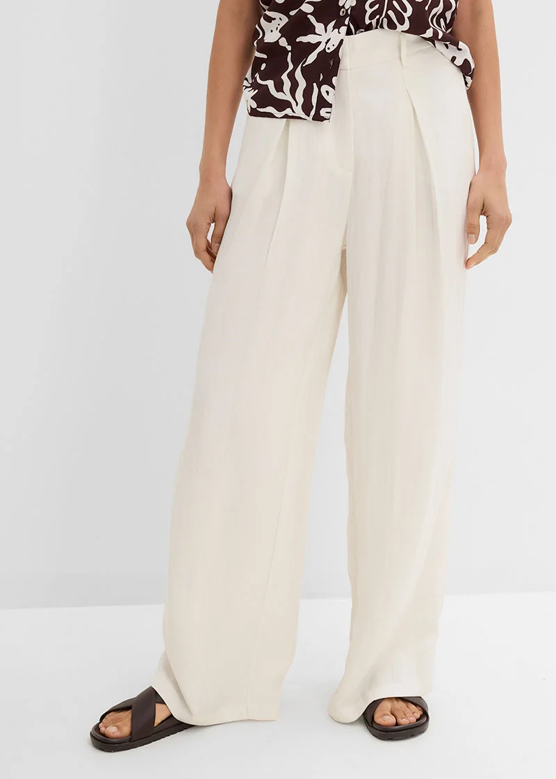 Pantalon large à plis de couleur claire, associé à un haut imprimé et des sandales confortables.