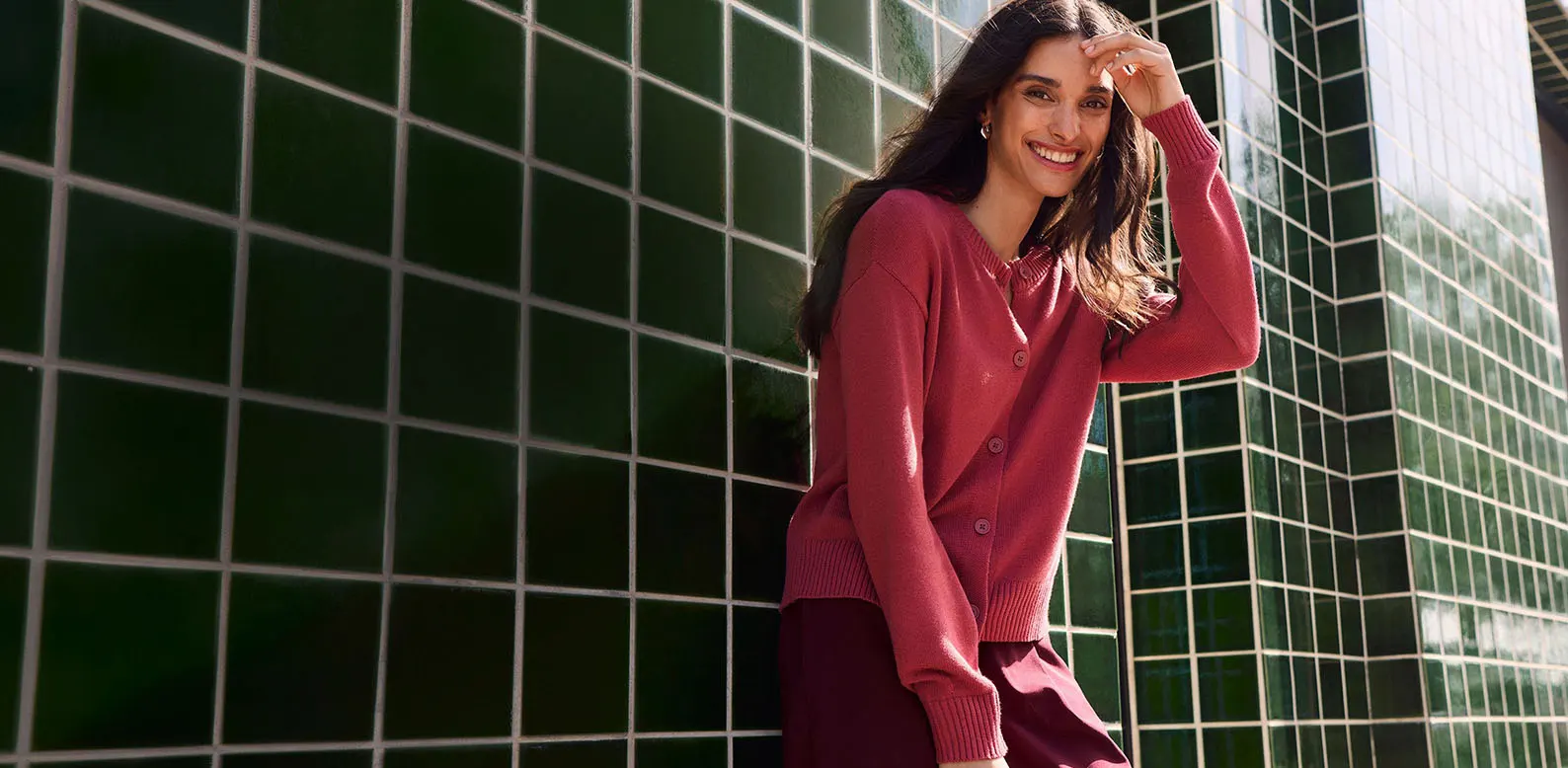 Une femme vêtue d'un cardigan fuchsia en maille et d'un pantalon large rouge bordeaux.