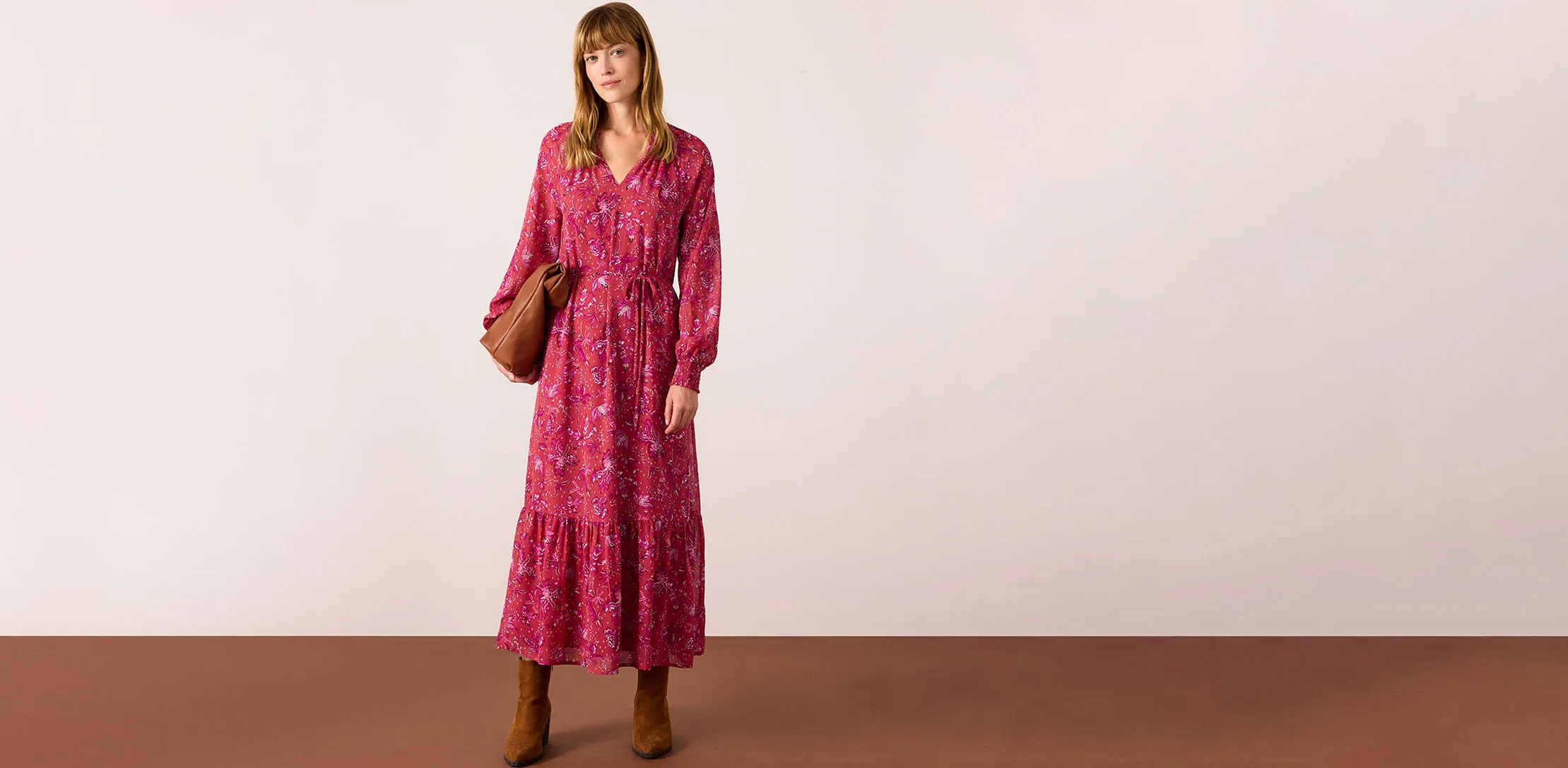 Robe longue rouge à motif floral, complétée par une paire de bottes marron et un sac à main.