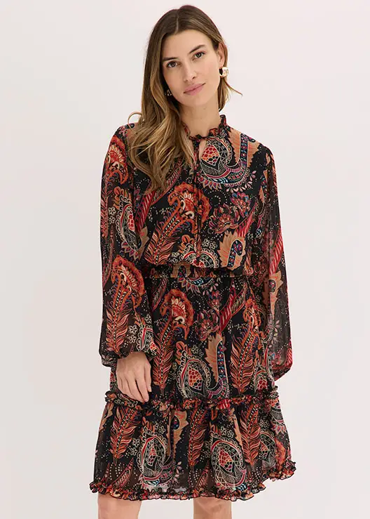 Une femme en robe fluide à motif paisley multicolore avec des détails ruchés.
