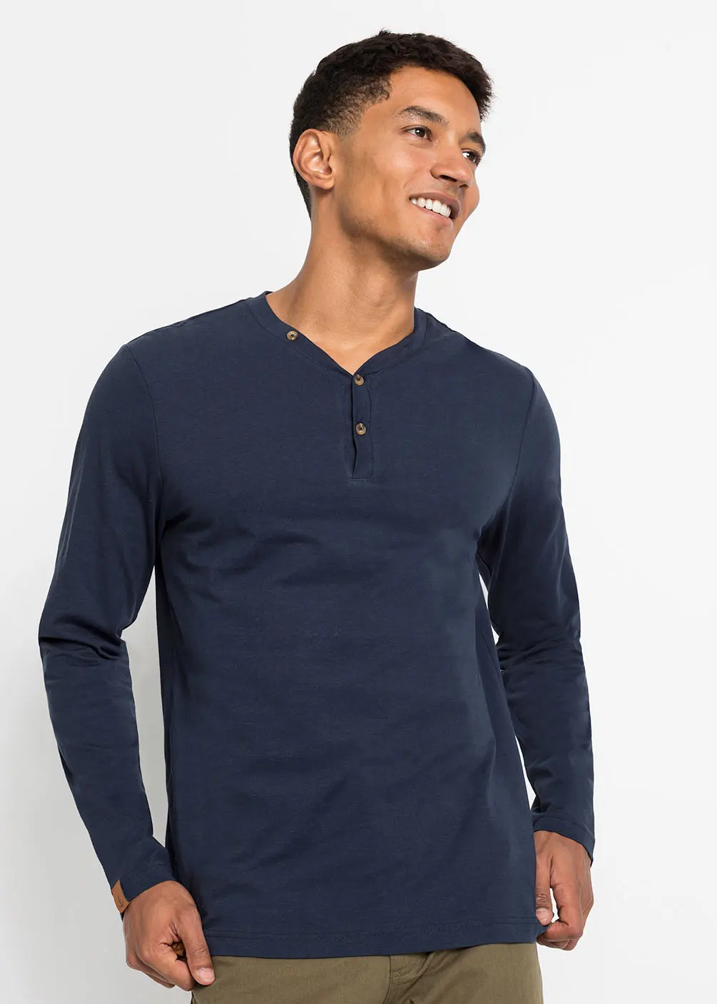 Un homme portant un T-shirt à manches longues bleu foncé avec une patte de boutonnage et un pantalon vert olive.