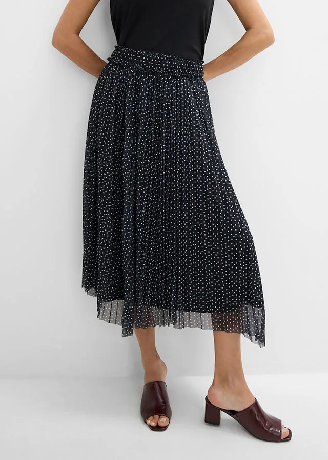 Top noir basique, jupe plissée à pois et mules marron foncé élégantes.