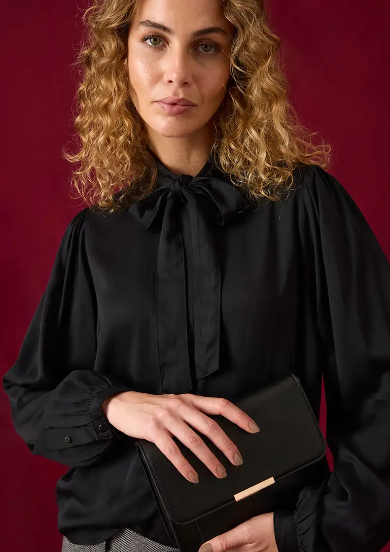 Chemisier noir à lavallière chic et manches amples, une pochette élégante complète la tenue.