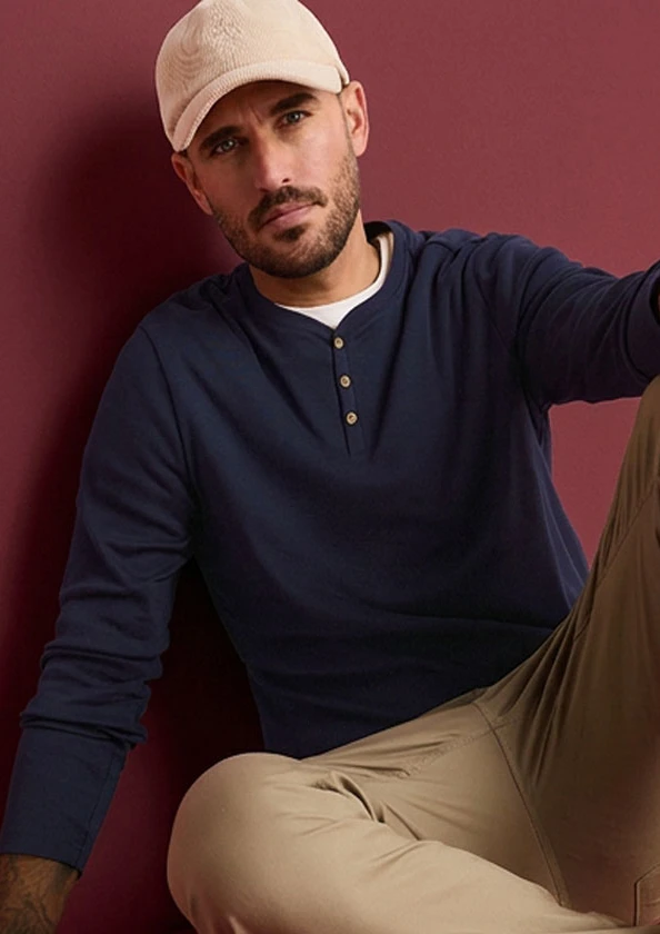 Homme portant une casquette beige, un T-shirt col tunisien bleu marine et un pantalon beige.