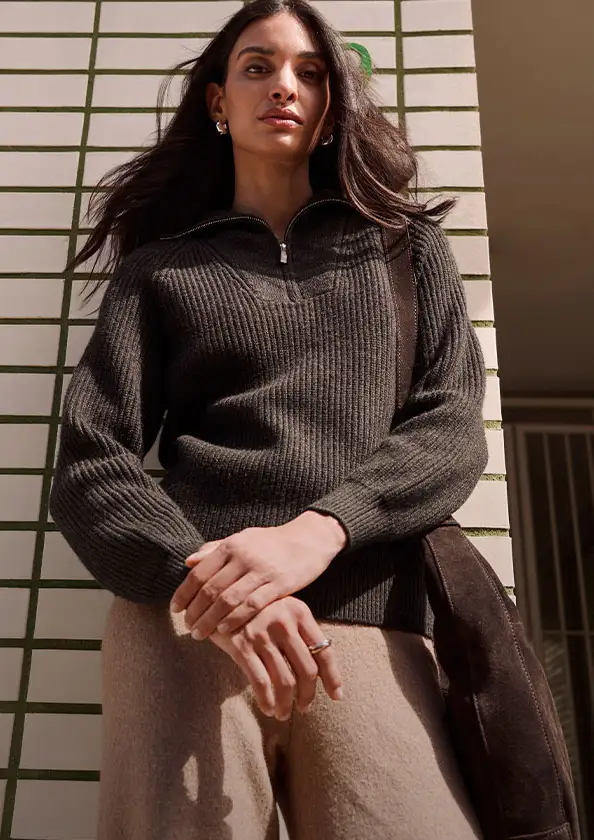 Pull en maille côtelée de couleur foncée avec un col zippé, pantalon clair et sac en daim marron.