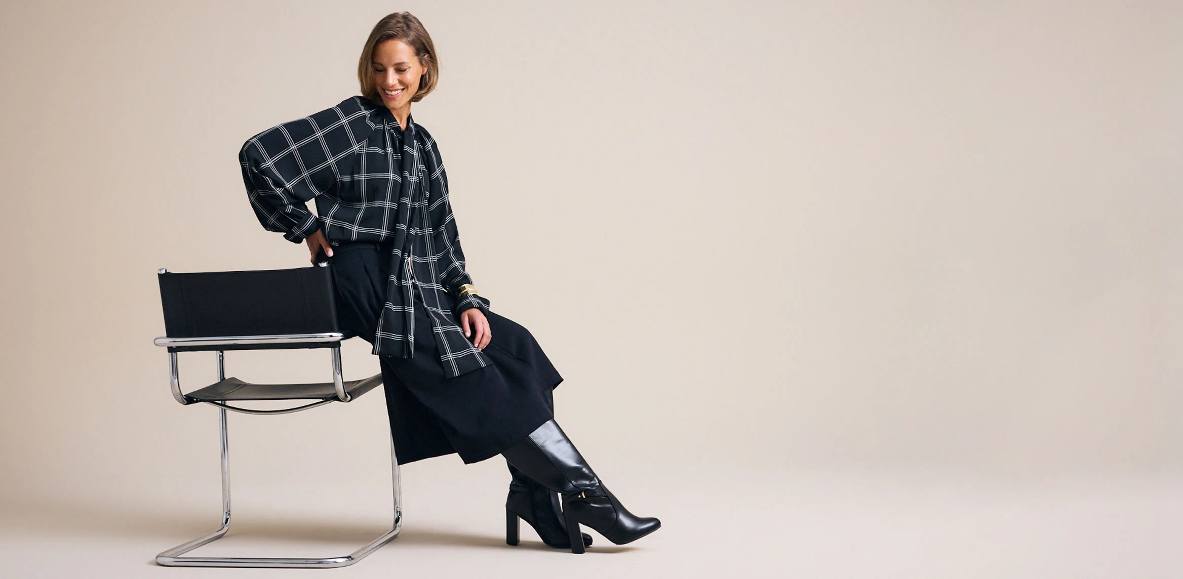 Tenue tendance avec une blouse à carreaux, un pantalon large et des bottes noires élégantes.