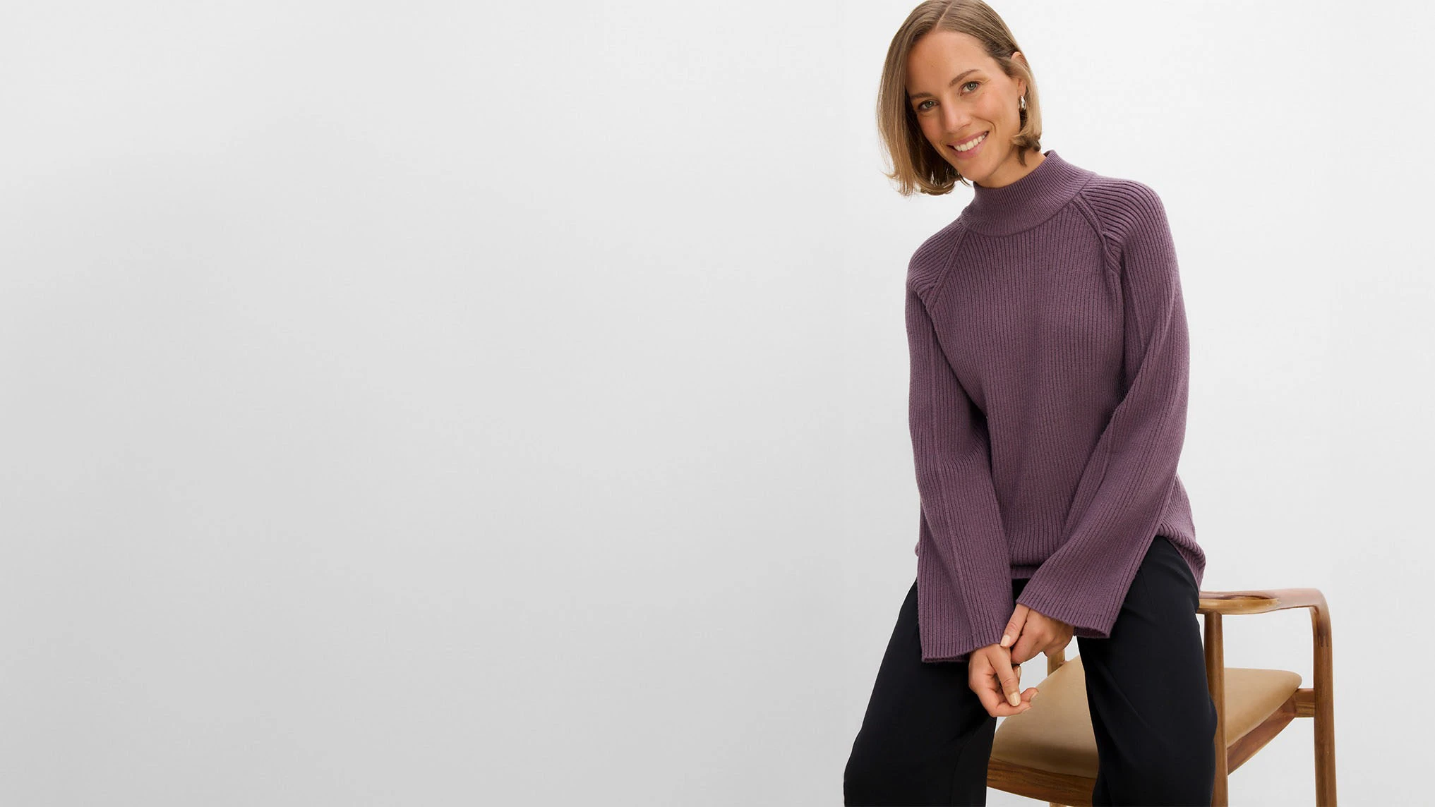 La femme porte un élégant pull à col roulé violet en maille côtelée et un pantalon noir.