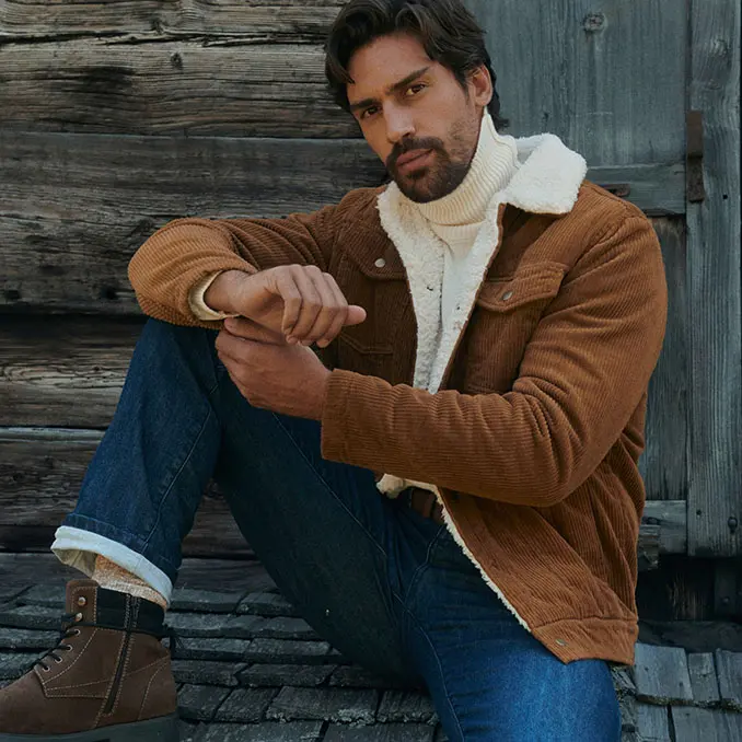 Un homme en veste en velours côtelée marron, pull à col roulé blanc, jean et bottes chaudes.