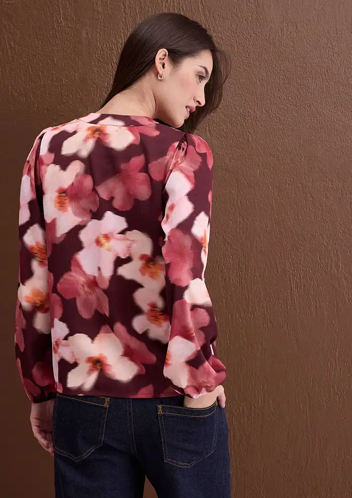 Blouse rouge foncé à motif floral raffiné, associée à un jean bleu foncé classique.