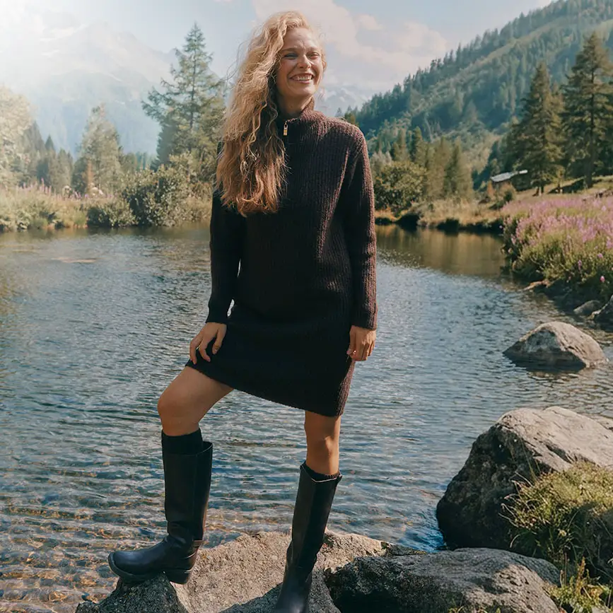 Femme portant une robe en maille marron foncé avec un col zippé, et des bottes noires.
